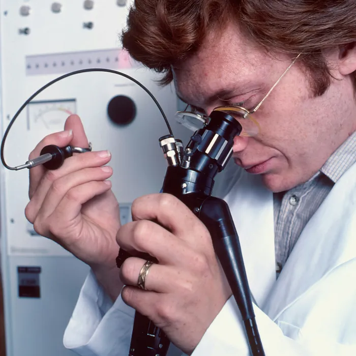 Ein männlicher Biologe, der ein ferngesteuertes Endoskop verwendet. Er schaut durch ein mikroskopähnliches Okular, um seine Handlungen zu überwachen, während er kleine Bürsten und Messer verwendet, um eine Biopsie durchzuführen.
