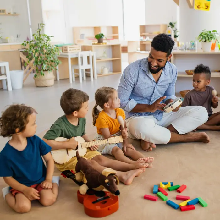 Erzieher in einer Elementar-Gruppe mit den Kindern auf dem Boden.