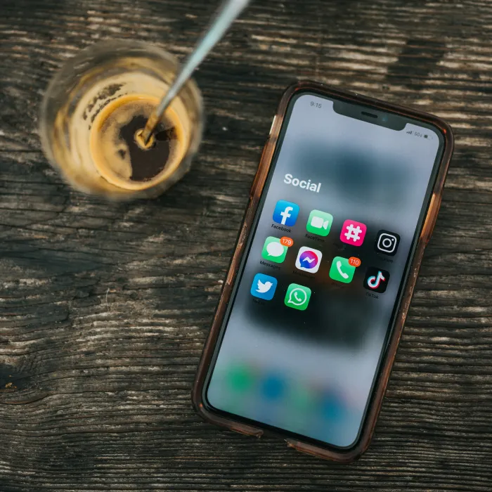 Handy auf dem Tisch neben dem Kaffee symbolisiert Social Media Management. Auf dem Handy sind Social Media Apps angezeigt.