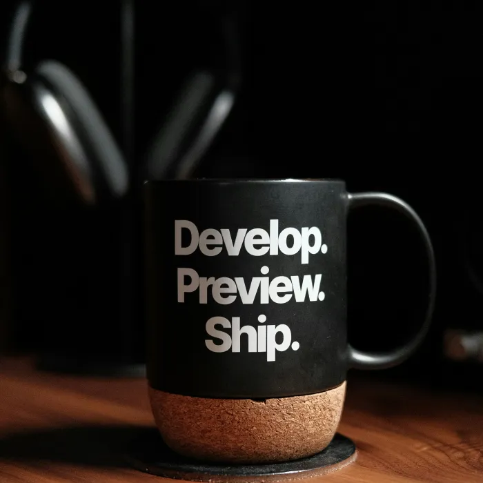 Schwarze Tasse eines UI / UX Designers auf dem Schreibtisch. Auf der Tasse steht: Develop. Preview. Ship.